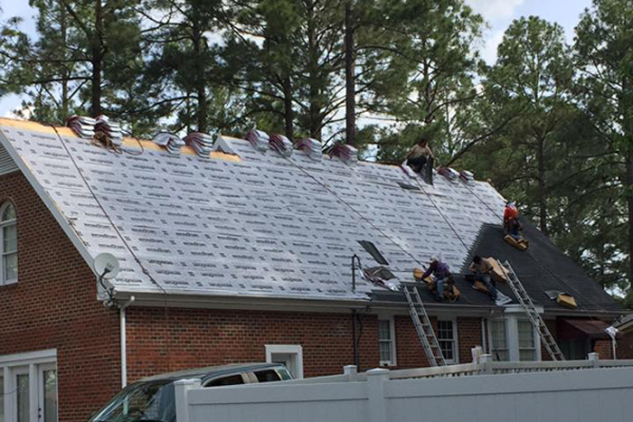 Men placing underlayment on a house roof to increase the average lifespan of the roof.